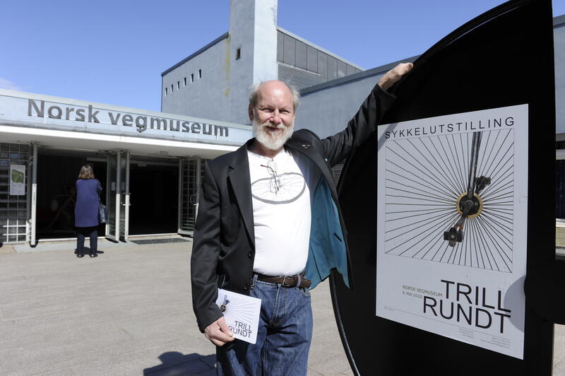 Einar Støp-Bowitz stående foran Norsk vegmuseum sammen med plakat for utstillingen Trill rundt.