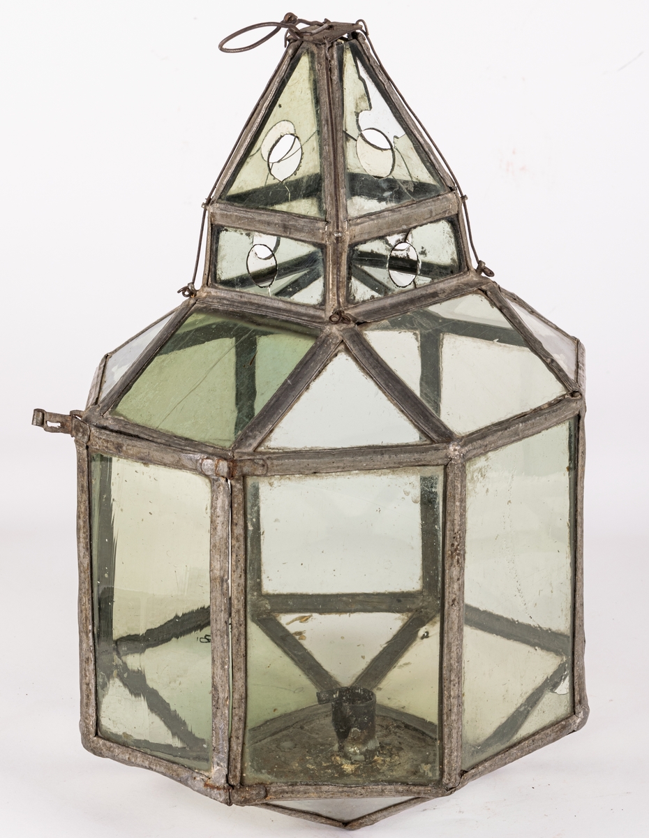 Lykta av glas med blyspröjsar emellan. 8-sidig med liten fyrsidig lanterning överst. Bottenstycke av plåt med hållare för ett ljus.