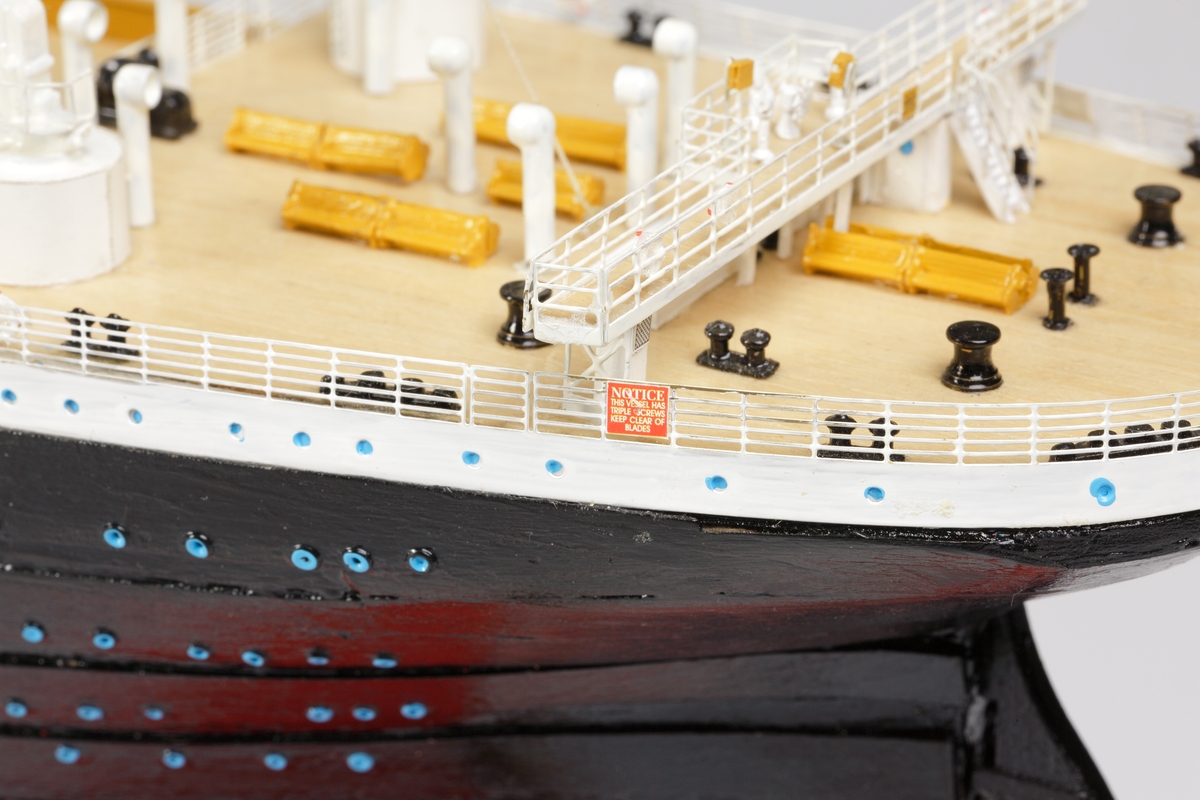 Oceanångare (Titanic) i trä och textil. Skrovet är målat i rött, svart och vitt, samt blått som är önsterventilerna. Däcket är trävitt och lackerat. På däcket finns detaljerat all utrustning såsom kranar, livbåtar, hytter, soffor och ventiler. Där finns fyra stora skorstenar med toppar i svart, och två större master med White Star Lines röda vimplar i toppen. Master och skorstenar är förbundna med linor i textil. I aktern är det tre propellrar och ett stort roder under vattenlinjen. Uppe vid relingen finns också en stång med en engelsk statsflagga. Modellen står på en brunbetsad platta i trä.