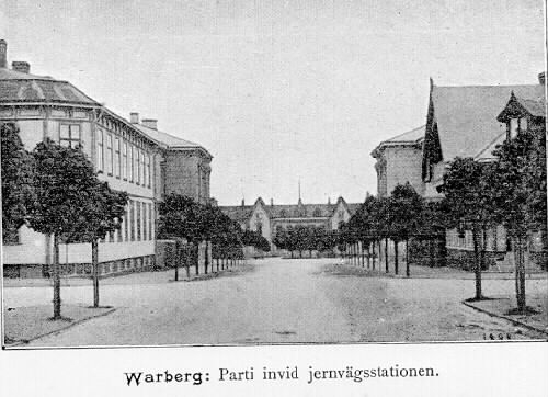 Vykort, "Warberg. Parti invid jernvägsstationen." Den avenyliknande (trädkantad och bredare än övriga gator) Eskilsgatan sedd mot järnvägsstationen i väster. Byggnaden till vänster närmast kameran kallas Adolfssonska fastigheten och ligger i kv Verkstaden; till höger kv Pipebruket.