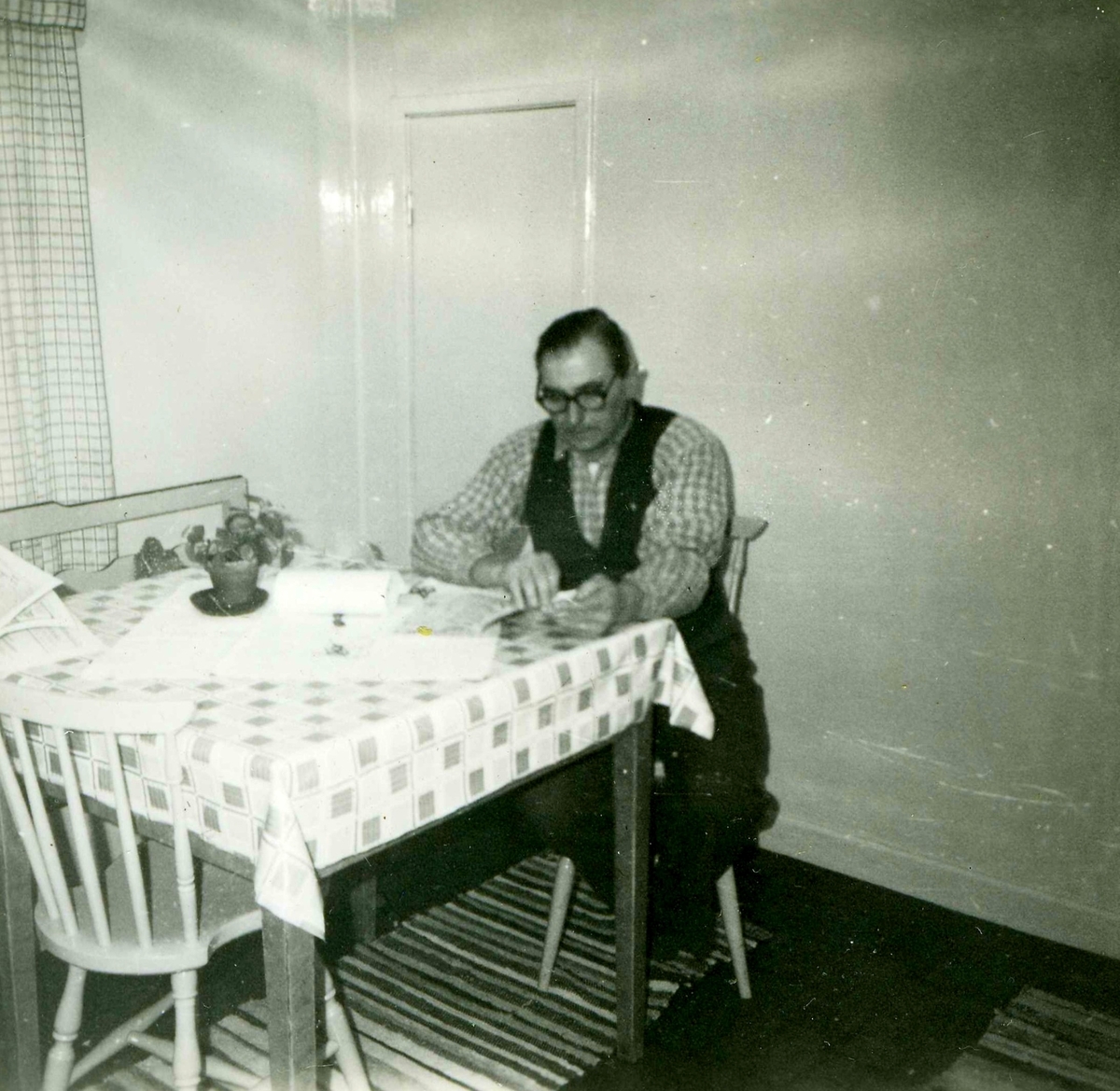 Erik Bengtsson (1899 - 1991) sitter och läser i sitt kök, Heljered Sörgård "Skräddarns" 1950-tal. Erik och och hustrun Margit drev jordbruk och ägde gården som senare revs. Sedan år 2013 ligger Heljereds förskola på platsen.