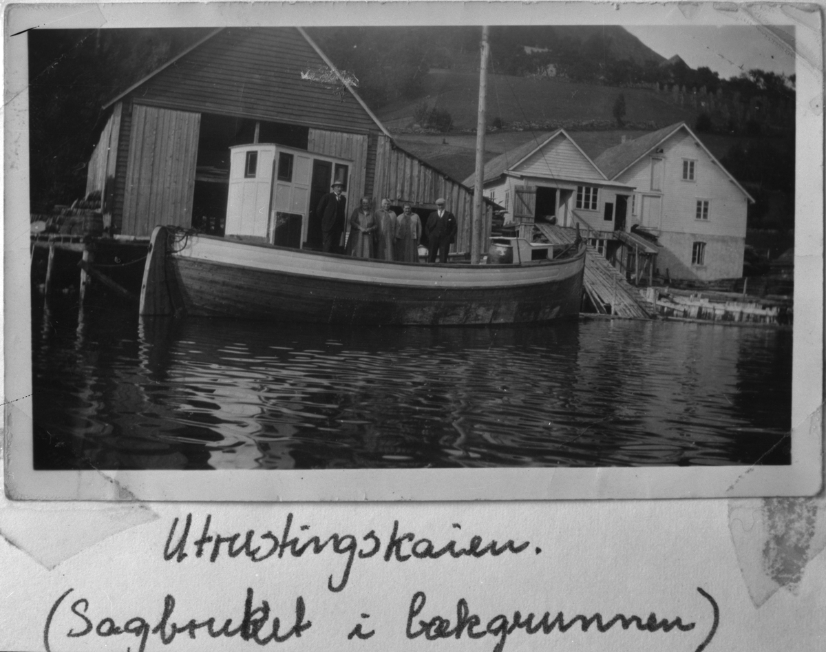 Utrustingskaien ved Berge Sag og Trelastforretning i Ølensvåg, ca. 1930. Sagbruket i bakgrunnen. Ombord i skøyta står, frå venstre: Knut Vaka, Sigrid Vaka, ukjend, fru Berge og Marselius Berge.