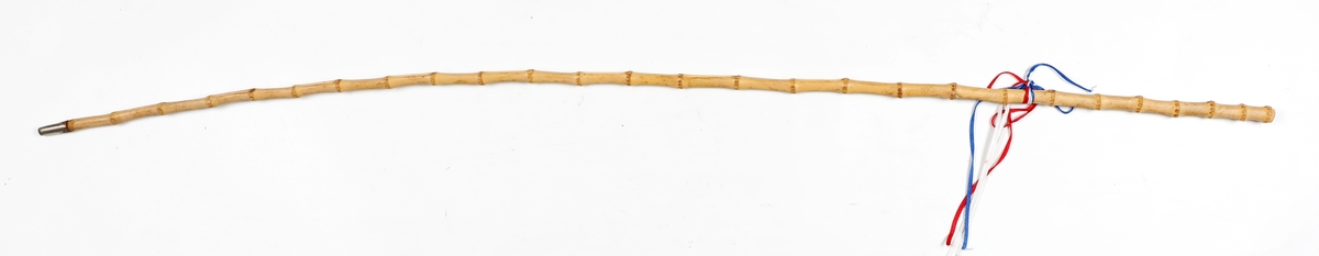 Bambusstokk med jerntupp og tynne bånd i rødt, hvitt og blått øverst.