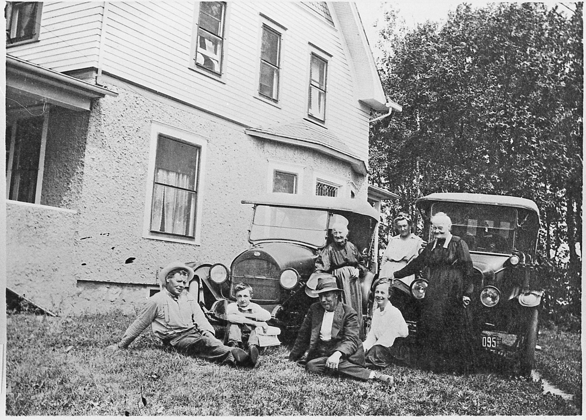 Ukjent familie, fotografert med automobiler foran en murvilla. Angivelig USA, august 1919.