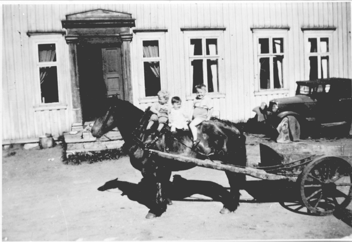 Tre barn sitter på hest utenfor våningshuset på Kulseng gård.