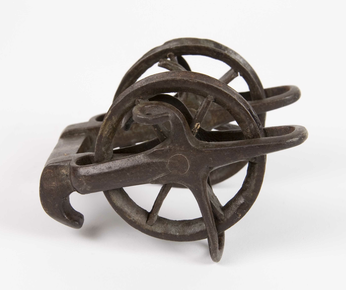 Armbrøstspenner av jern. To løpehjul i jern montert på en skaling med bro med to påsmidde haker for feste av buesnor.