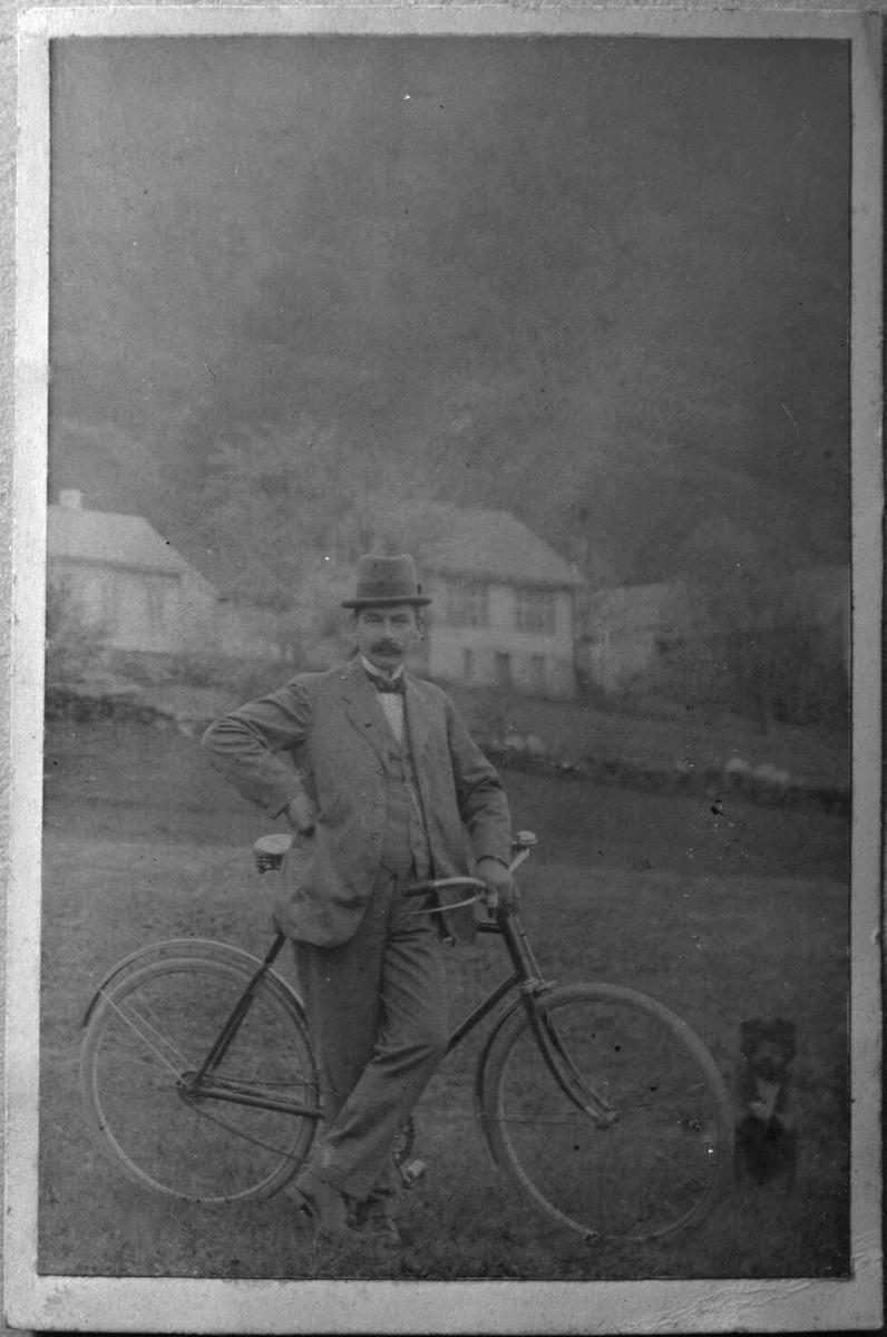 Nils Fadnes med sykkel ved Dørheim i Ølen, ca. 1920. Til venstre i bakgrunnen er verkstad og stovehus på garden til Nils Fadnes. Til høgre i bakgrunnen er løa og stovehuset til Ole Helland.