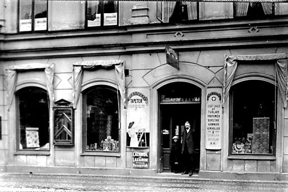 Fasad av byggnad; skylt med text "A:B WILH. BÄCKMAN FÄRGHANDEL". I förgrunden står en man och ett barn.
Firman startades 1893 av direktör Wilh. Bäckman som en mindre färghandel. Dess första lokaler låg vid Östra Torggatan. Firman hade därefter lokaler i Hotell Grands fastighet, och efter 10 års verksamhet flyttade företaget in i en egen fastighet. De första åren omfattade  verksamheten försäljning endast av färger och oljor, men efterhand upptogs även andra artiklar. Största intresset ägnades dock åt detaljhandeln. År 1924 ombildades firman till aktiebolag med Wilh. Bäckman som verkställande direktör. Efter hans död blev Adolf Edenholm, som varit anställd sedan 1901, chef för verksamheten.
Källa: Nyblom-Svanqvist, Näringsliv i Värmland, 1945.