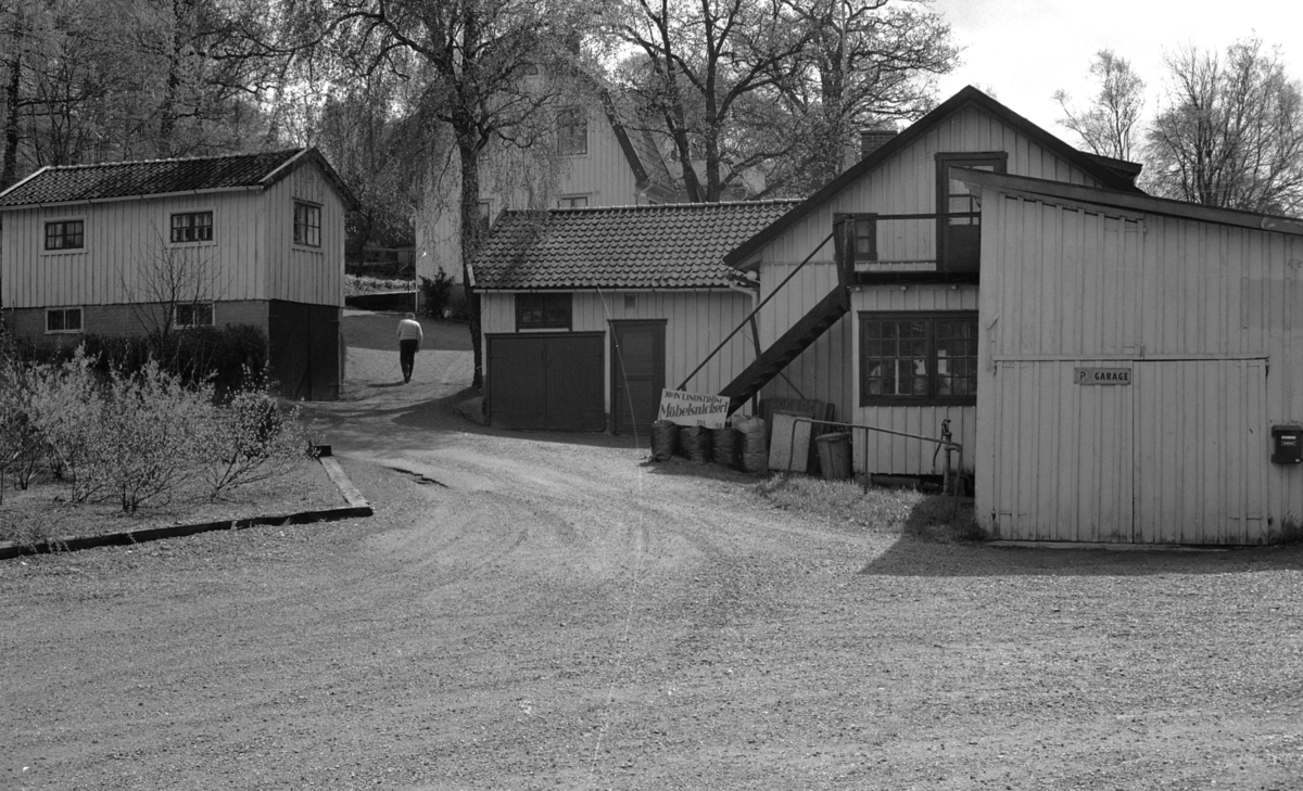 John Lindström Möbelsnickeri vid Ekebacken på Gamla Riksvägen 79 (nu: Gamla Riksvägen 81), 1980-tal. Till vänster ligger Lillstugan. I mitten boningshuset med två lägenheter. Till höger snickeriet med garage. Skylten finns nu i Hembygdsföreningens samlingar. Notera i mitten hur taket har ändrats efter björken. John Lindström promenerar upp mot bostaden.