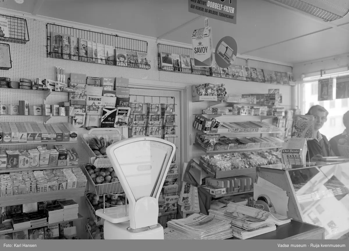 Narvesen kiosk, Vadsø 13.mai 1965. Deler av interiøret og vareutvalget i kiosken. Kioskansatte Pauline (Bølla) Stock og Anny Iversen.