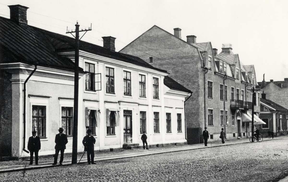 Kronobergsgatan, Växjö, med kvarteret Nordstjernan nr 2-3. Tidigt 1900-tal.
Några herrar poserar för fotografen på trottoaren. Man skymtar också några hus i kvarteret Lyktan i bakgrunden.