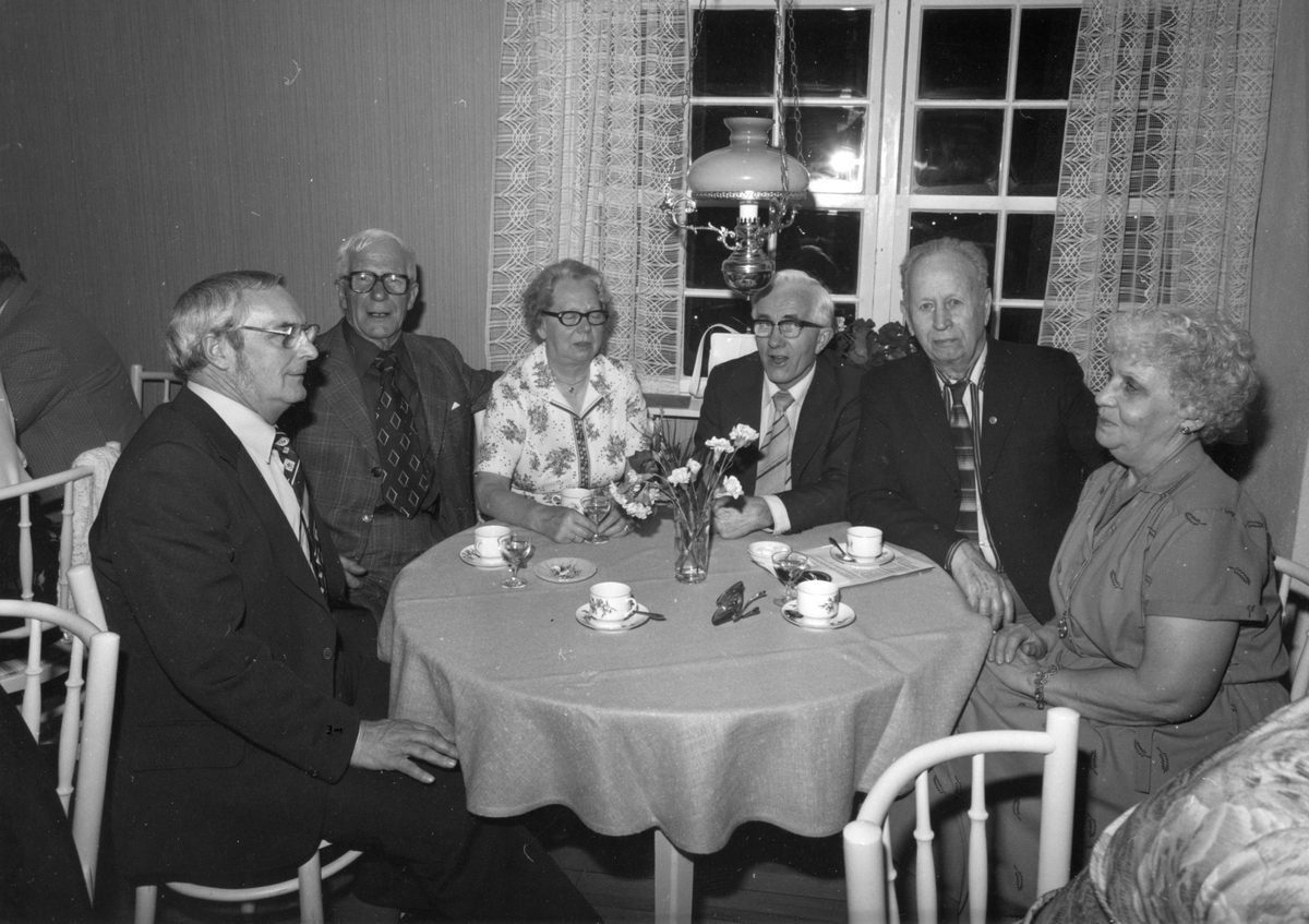 Två kvinnor och fyra män sitter runt ett bord och dricker kaffe med avec.