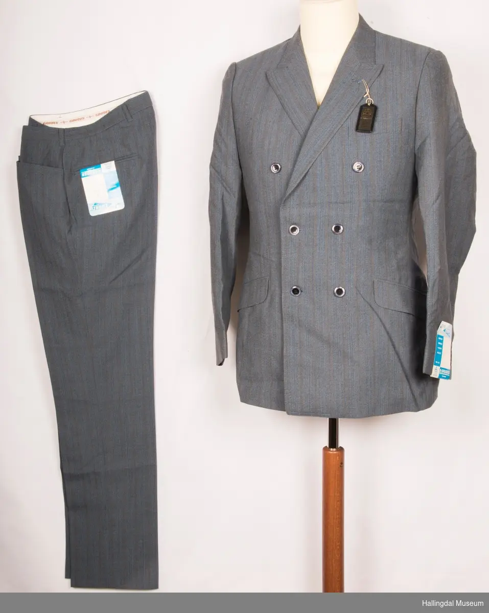 Grå herredress med jakke og bukse fra K. Grudes konfeksjonsfabrikk AS.  Dobbeltspent dressjakke med 3 knapper og knapphull på hver side.