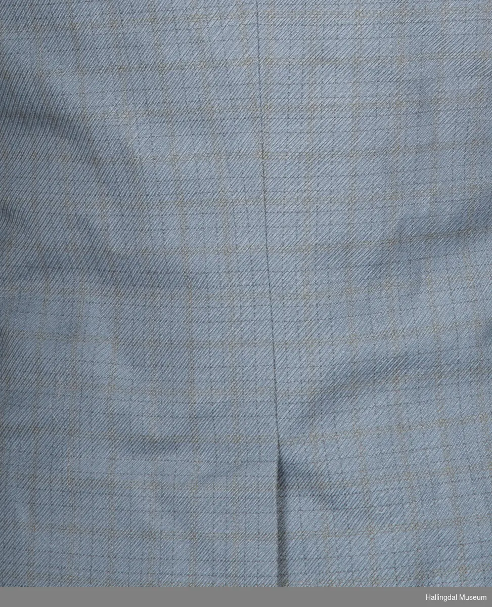 Grå herredress med jakke og bukse fra K. Grudes konfeksjonsfabrikk AS.  Dobbeltspent dressjakke med 3 knapper og knapphull på hver side.
