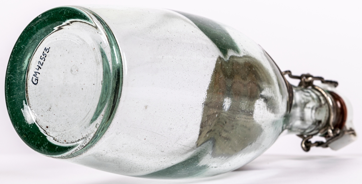 Flaska av genomskinligt glas, bukig form. Patentkort av keramik. Klistrad pappersetikett: Engelskt sodavatten, Mineralvattenfabriken Gevalia, Gefle