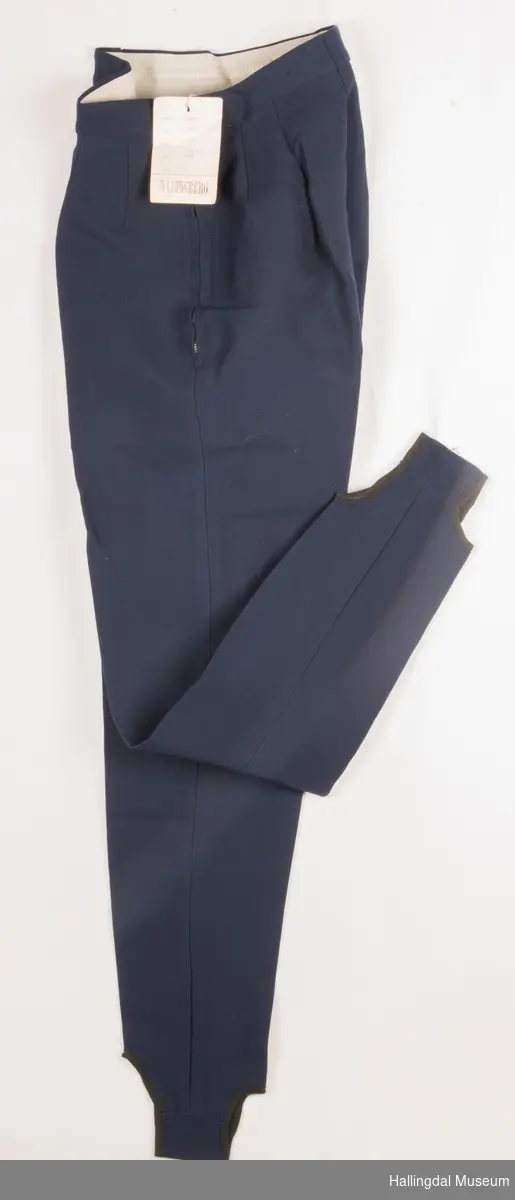Mørk blå strekkbukse med glidelås i venstre side.  Fotstroppen er i samme tøy som buksa. Ingen lommer.