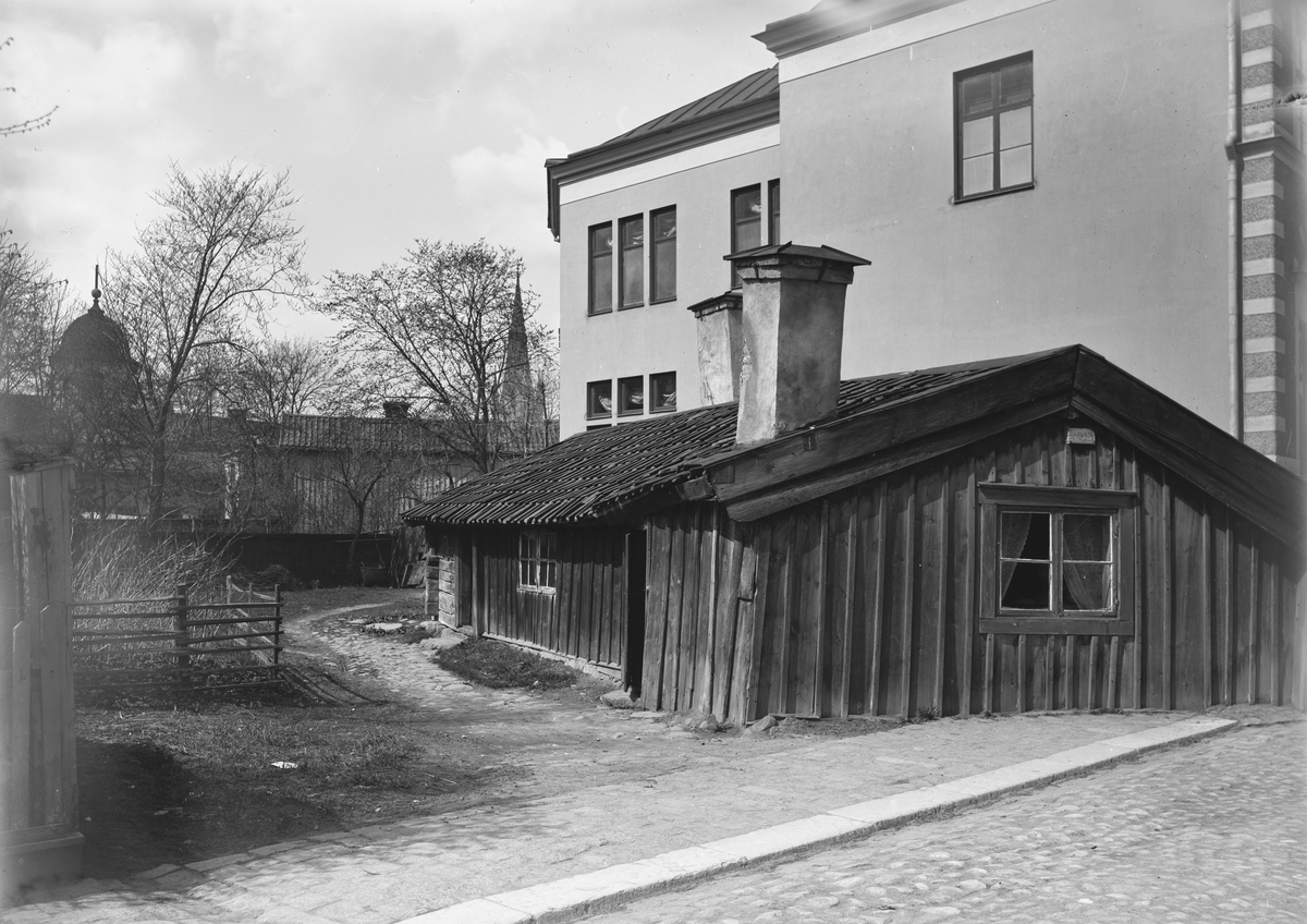 Klostergatan 13 (nuvarande nr 48) i Linköping. Låg ryggåsstuga som länge (revs 1935) bredde ut sig på gatans trottoar. Byggnaden till höger är Betaniakapellet. I fonden skymtar tornen till både Hospitalskyrkan och Domkyrkan. Den förstnämnda kyrkan revs 1897 vilket ger senast, möjliga datering.