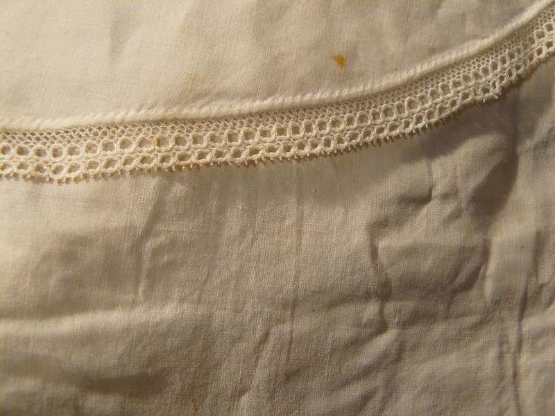Kjolekrage av hvitt stivet bomullsstoff med blondekant. Har skulder og forstykke med snorer. Tvinnet bomullsnorer nedre kant på bakstykket og bomullbåndhemper i forstykkene.