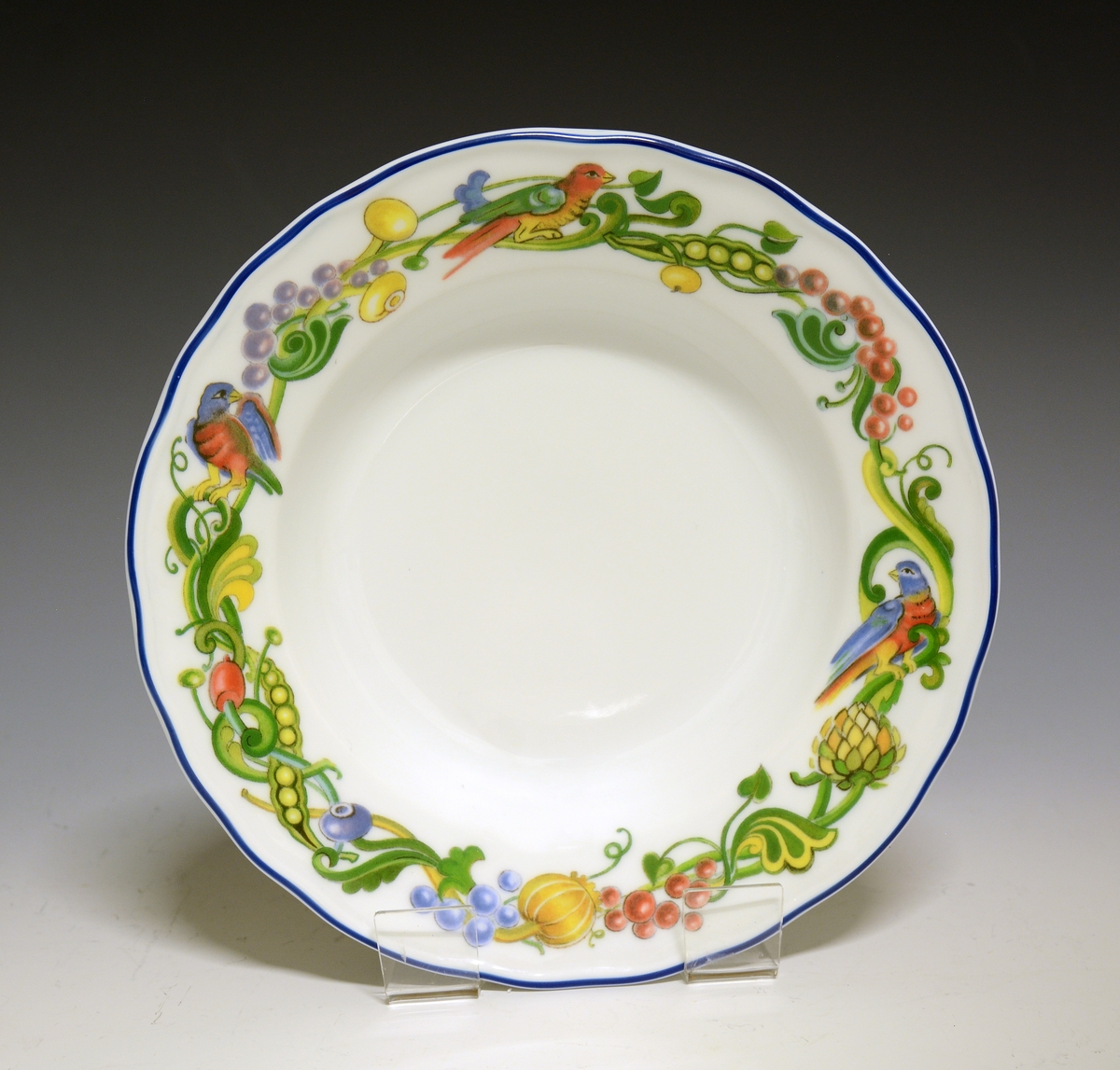 Tallerken av porselen med hvit glasur. Dekorert med en bord rundt fanen med fugler, bær og bladverk.
Modell: Victoria
Dekor: Fantasia