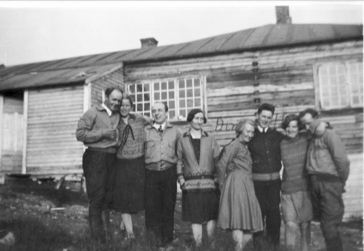 Gruppe på fire menn og fire kvinner stående utenfor hytte/turisthytte.