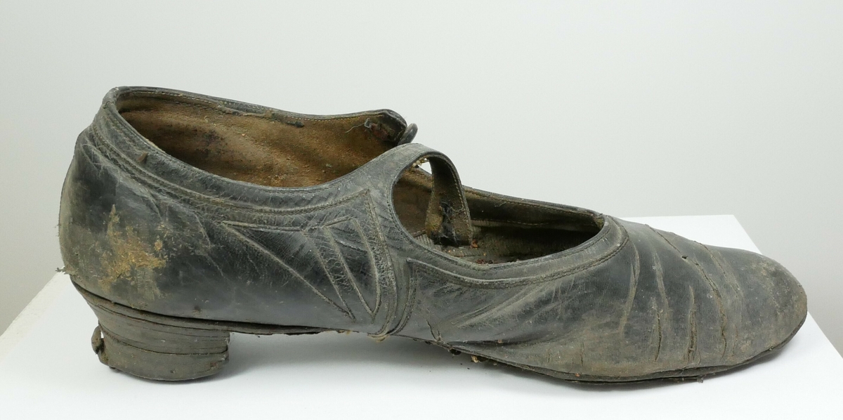 Ett par svarte sko med en hæl og reim. 