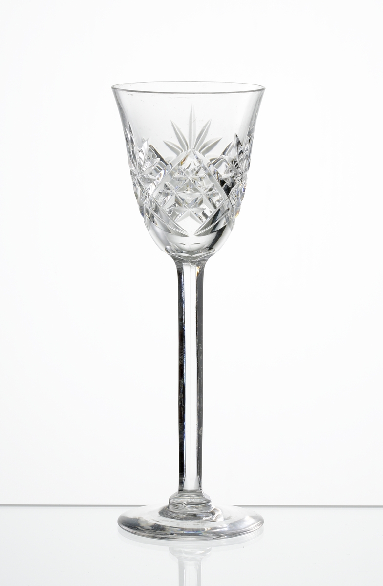 Design: Okänd. 
Brännvinsglas, lätt klockformad kupa med skärslipad dekor. Högt fasettslipat ben med slät fot.