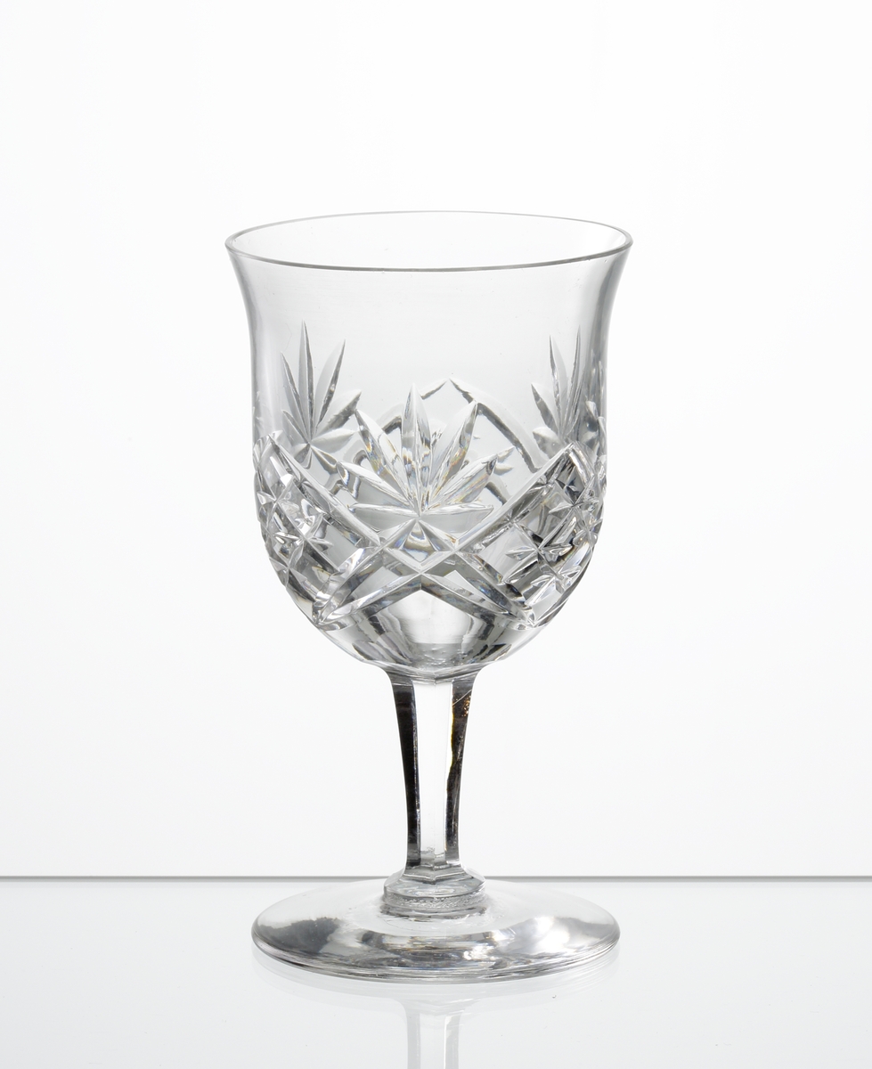 Design: Okänd. 
Portvinsglas, lätt klockformad kupa med skärslipad dekor. Lågt fasettslipat ben med slät fot.