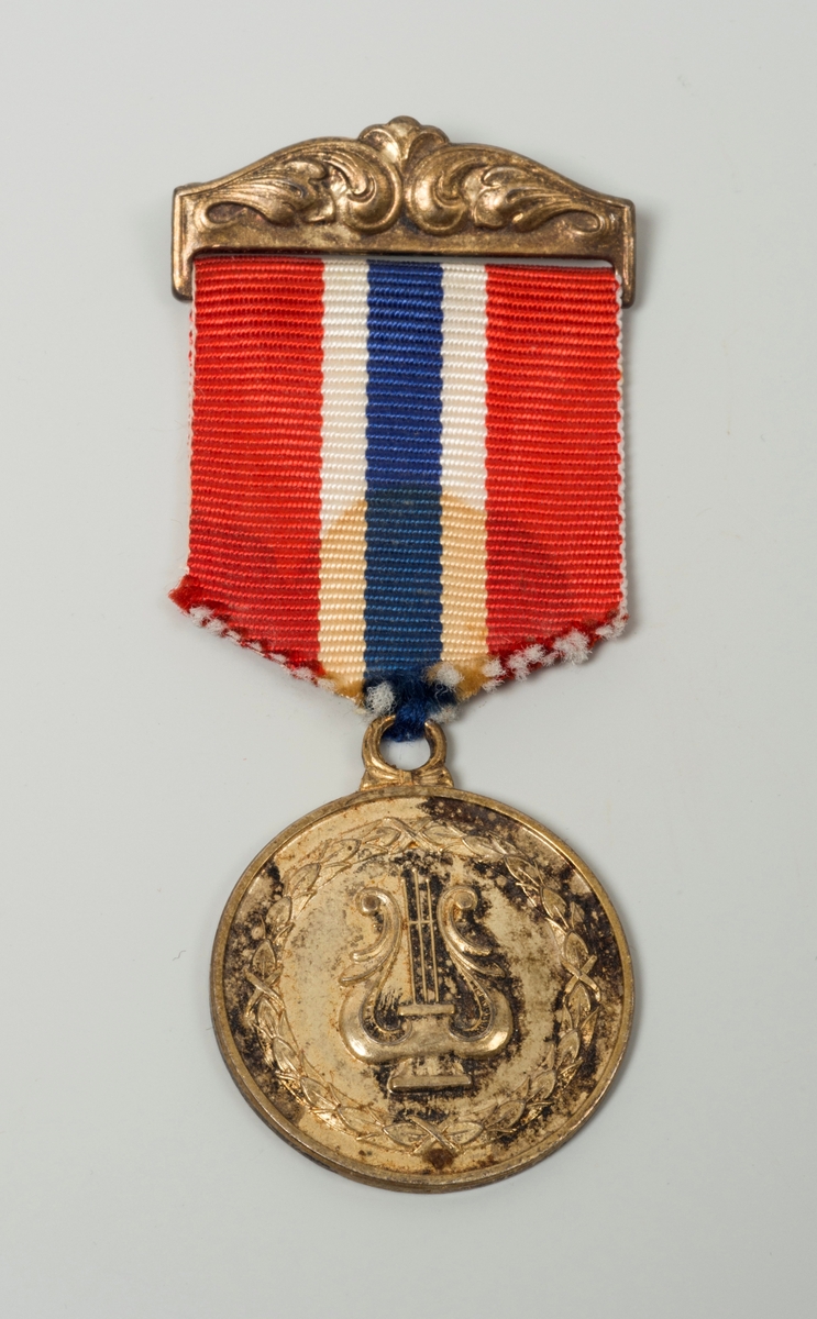 Medalje med ekegrener og harpe, med sløyfe i det norske flaggs farger.