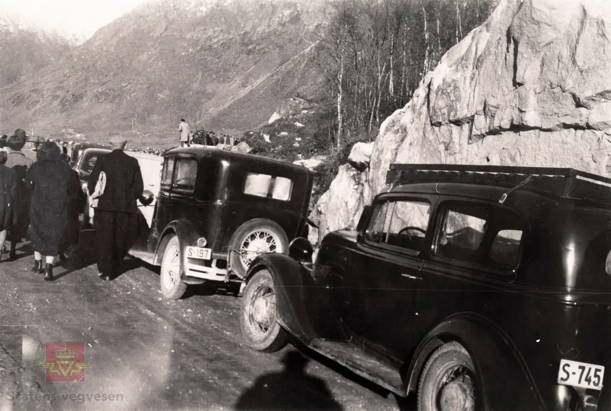Opninga av fylkesveg 337 Hafslo-Veitastrondi på Stølsneset ved Kvam, 20. oktober 1956.

Vegen blei opna av fylkesmann Nikolai Schei (1945-1971) og vegsjef Egil Abrahamsen (1956-1970). 

To bilar med kjennemerke "S-197" og "S-745" står parkert langs med vegen.

Bil med kjenneteikn S-197 er ein Ford A, frå  år 1930-31 og S-745 kan være ein Chevrolet 1934-modell.

(Informant: Ivar E. Stav.) 