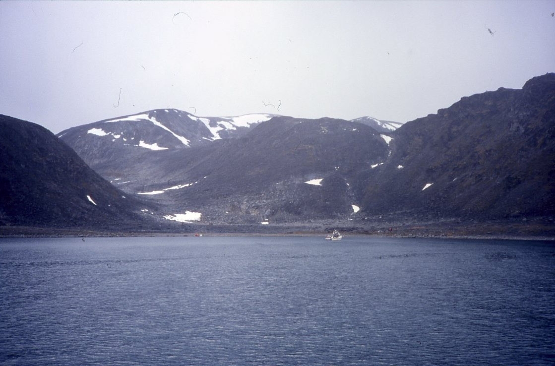 En bergskedja på Danskön med Wellmankollen till vänster, nedanför vilken S A Andrées polarballong lyfte ifrån. En mindre båt ligger ankrad nära stranden.