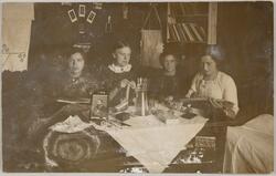 Postkort med bilde av fire kvinner. De sitter rundt et bord 