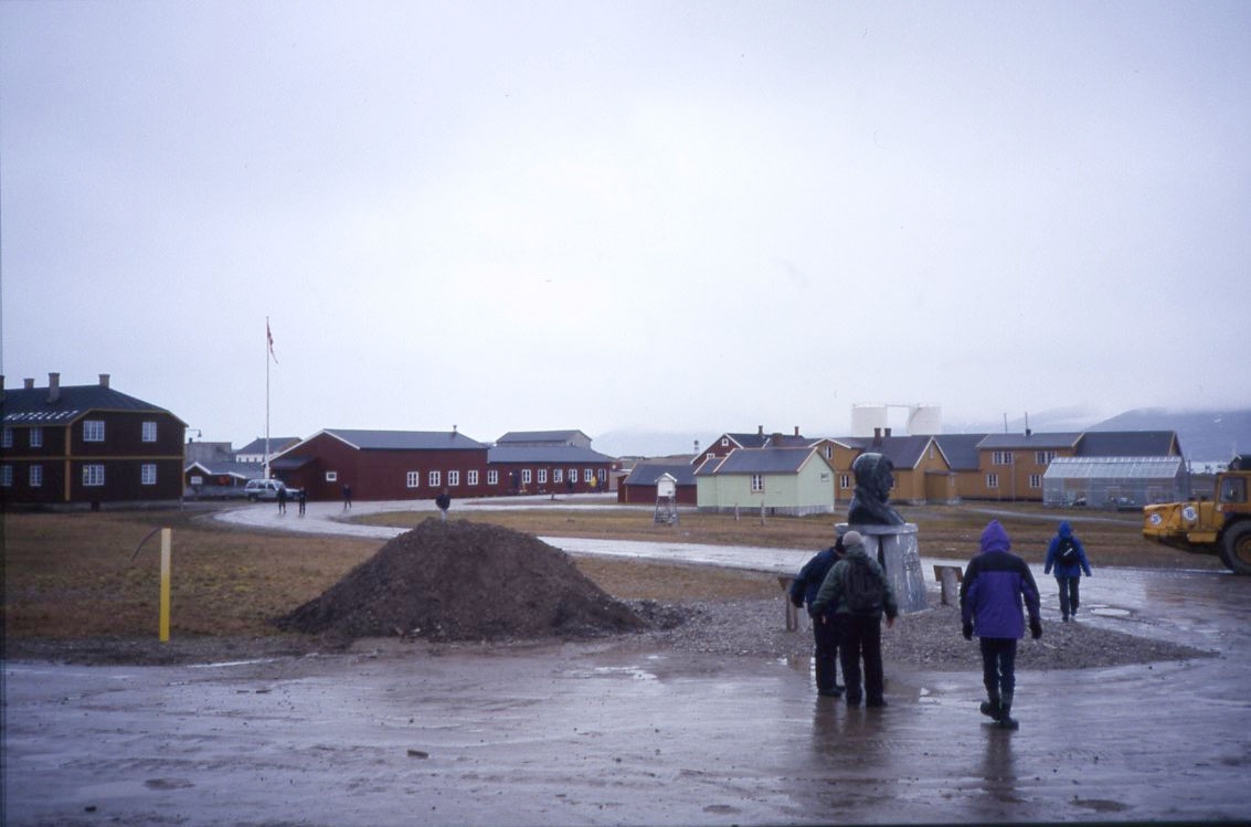 En grå dag i Ny-Ålesund. Ett litet turistsällskap vid en Amundsen-byst.