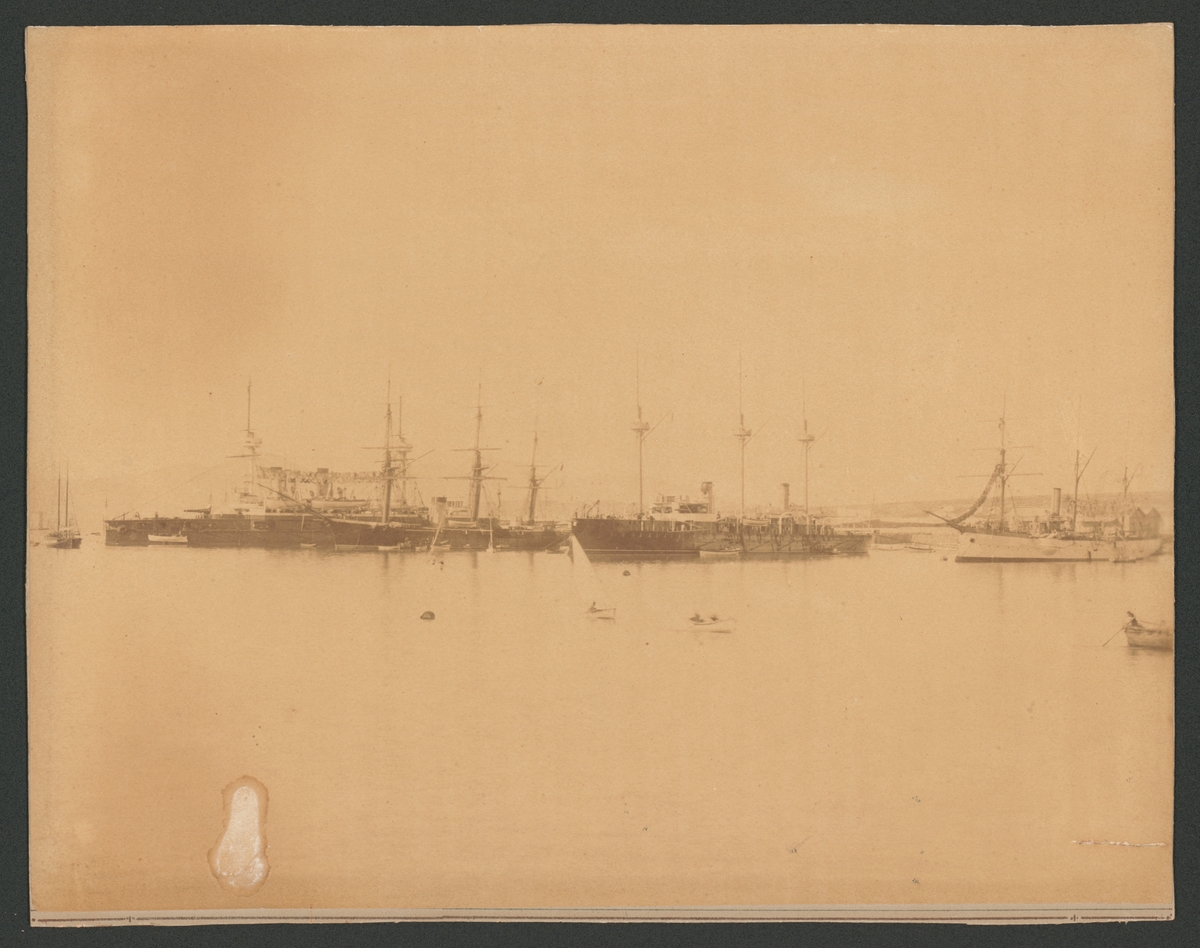 Bilden föreställer ångkorvetten Balder som ligger till ankars i Pireus bredvid tre andra örlogsfartyg. Fartygets syns från babordssidan med bärgade segel. Framför skeppet pågår en livlig trafik med skeppsbåtar.