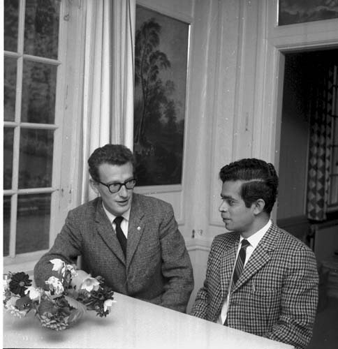 Rektorn för Grännaskolan, Sten Sarborn sitter och samtalar med en man. Båda klädda i slipsar. Framför dem på bordet står en bukett blommor.