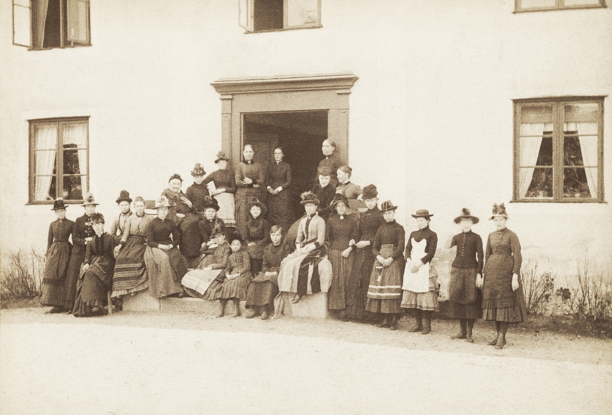 Kampagården (Kampen), Växjö landsfs, 28 maj 1886. 
En stor skara kvinnor och flickor har samlats vid huvudingången till Kampagården, kanske för att fira den äldre dam 
som sitter högst upp till vänster på trappan.