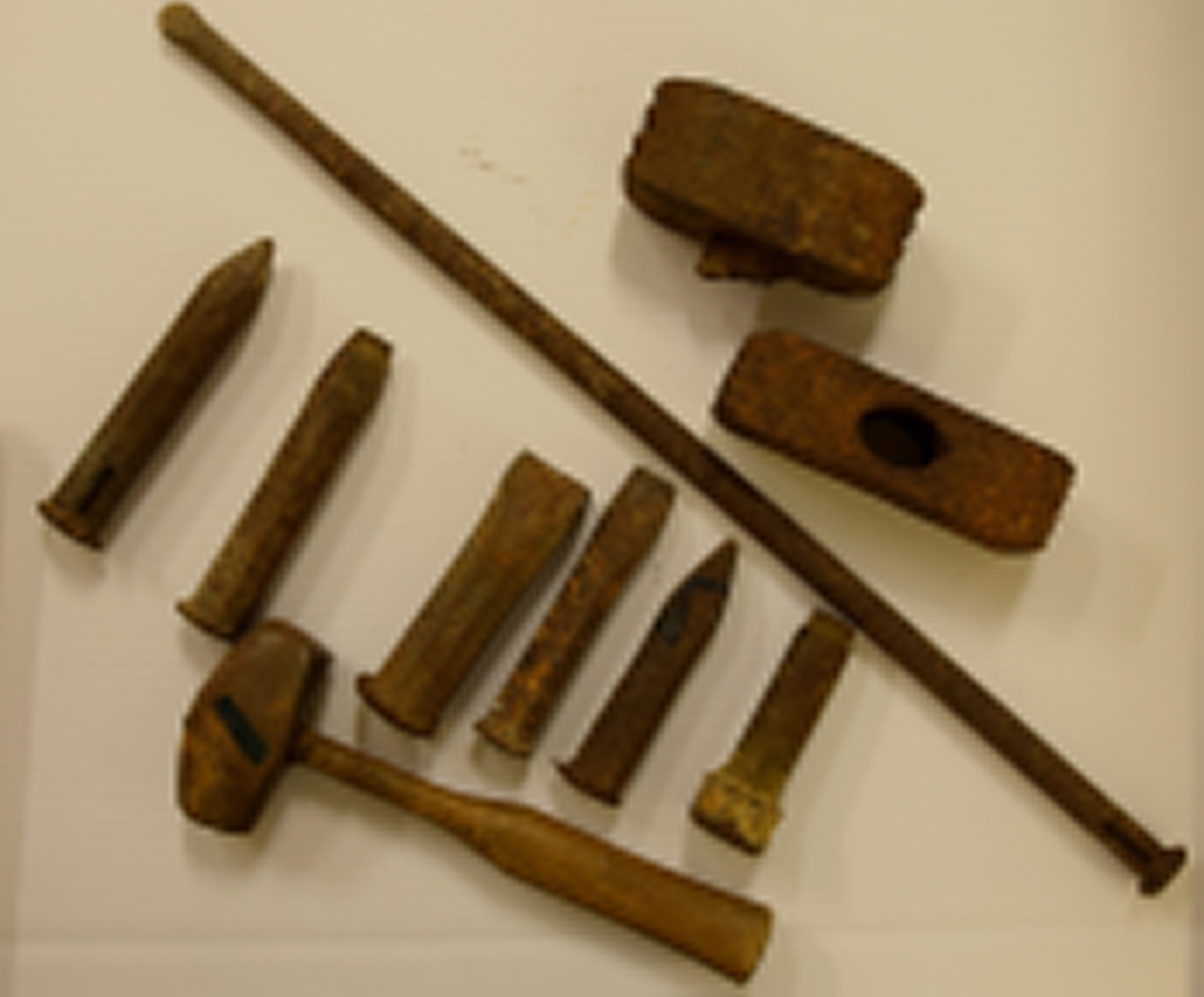Steinhuggerverktøy i jern som består av ti deler, en hammer/slager med treskaft, to prikkhammere, hvorav en har rester av treskaft og syv meisler.