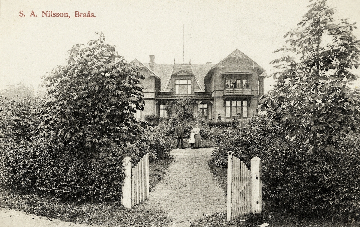 S.A. Nilsson, Braås. En större villa med trädgård, ca 1900. En man och en kvinna står framför huset med sin dotter.