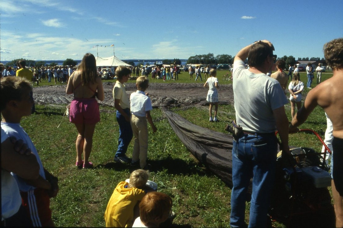 Ett stort brunt ballonghölje ligger utlags på en gräsplan. Det är kopian av Andrées ballong Örnen från Jan Troells biofilm "Ingenjör Andrées luftfärd". Barn och vuxna runtomkring.