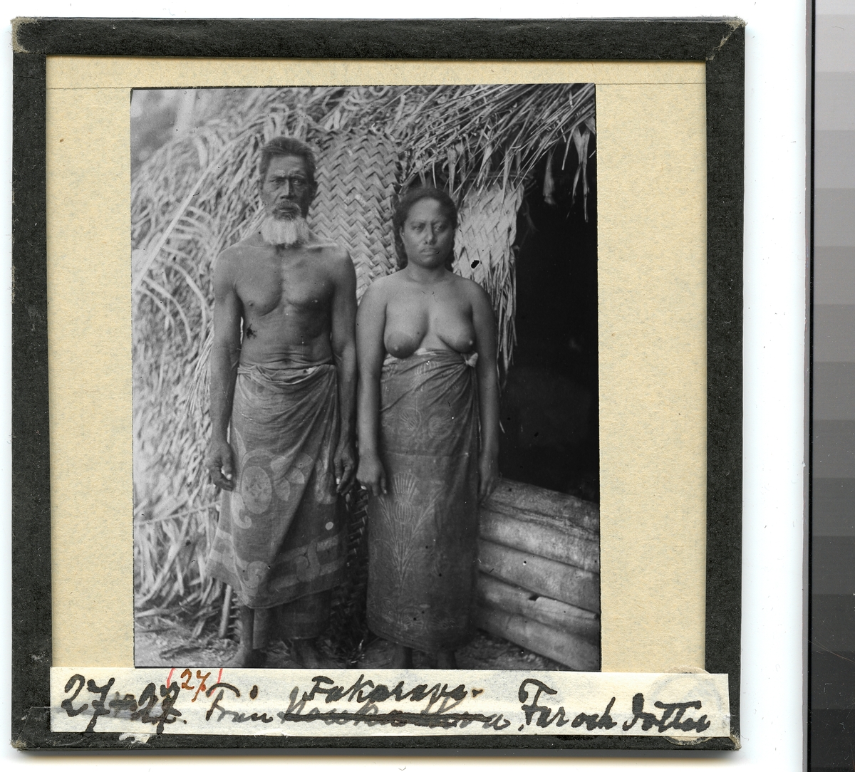 Bilden visar en man och en kvinna från ursprungsbefolkningen på Fakarava klädd i en traditionella dräkter som står framför en hydda. Enlig Etnografiska museets bildinformation är det far och dotter, Tairi och Taroi.