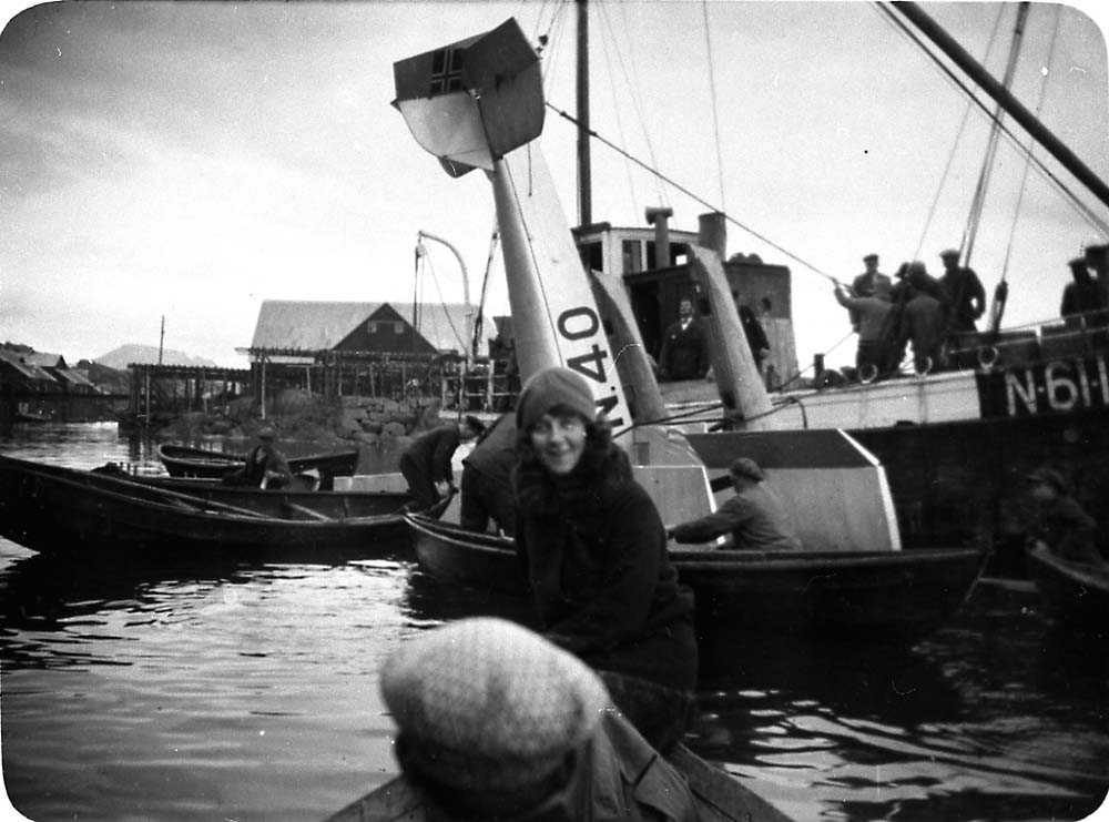 Ett sjøfly som heises ombord i en båt etter berging, Saaski "Måsen" Flere båter rundt med flere personer i. Bygninger i bakgrunnen.