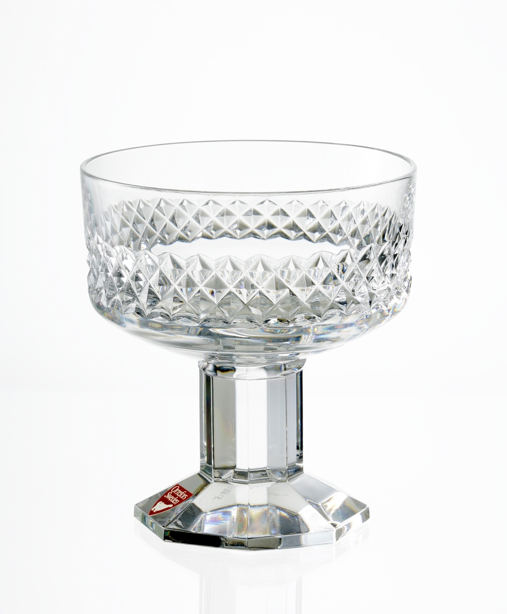 Design: Nils Landberg.
Champagneskål. Cylindrisk kupa med diamantslipad dekor på kupans nedre del. Fasettslipat lågt ben. Fasettslipad, åttkantig fot.