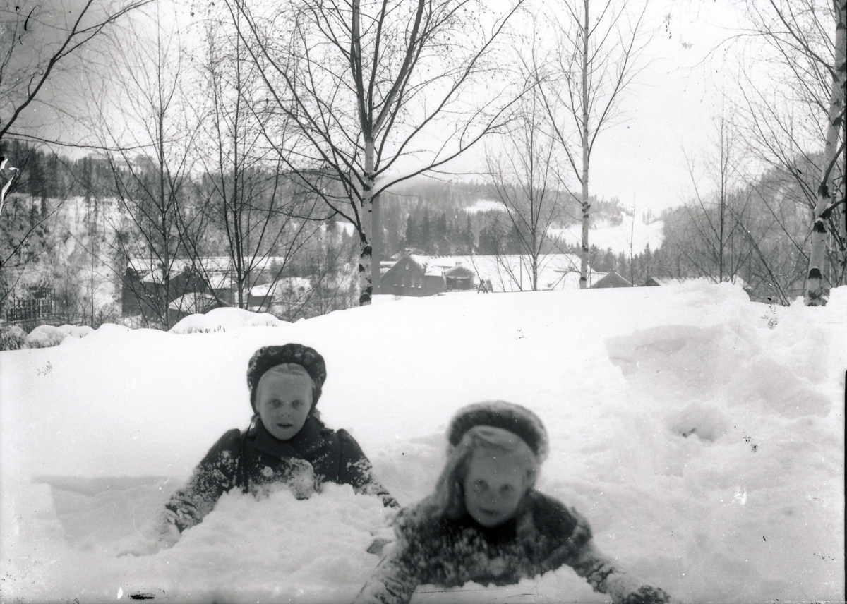 Eia og Lisbeth Rydgren leker i snøen utenfor bestyrervillaen på Kistefos. Industribygninger og skog i bakgrunnen.