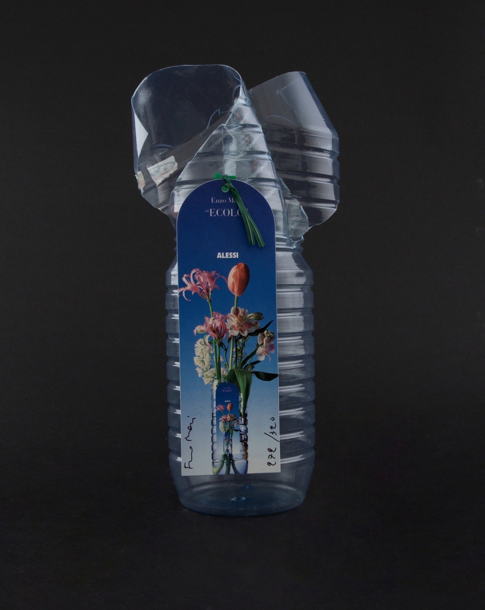 Vase av vannflaske i plast. Kort med bilde av blomster i vase er festet til vasen med et grønt feste.