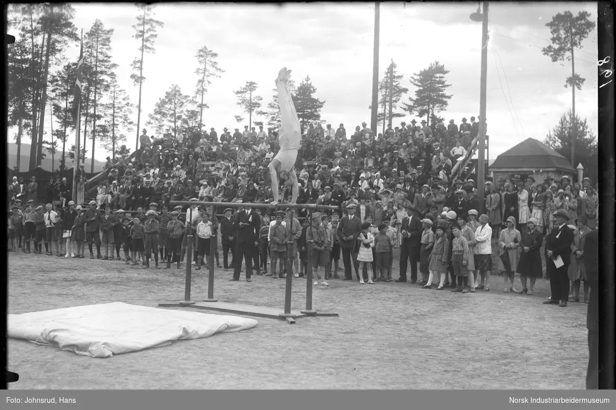 Kretsturnstevne 1930. Mann i øvelse skranke. Publikum står rundt idrettsanlegget.