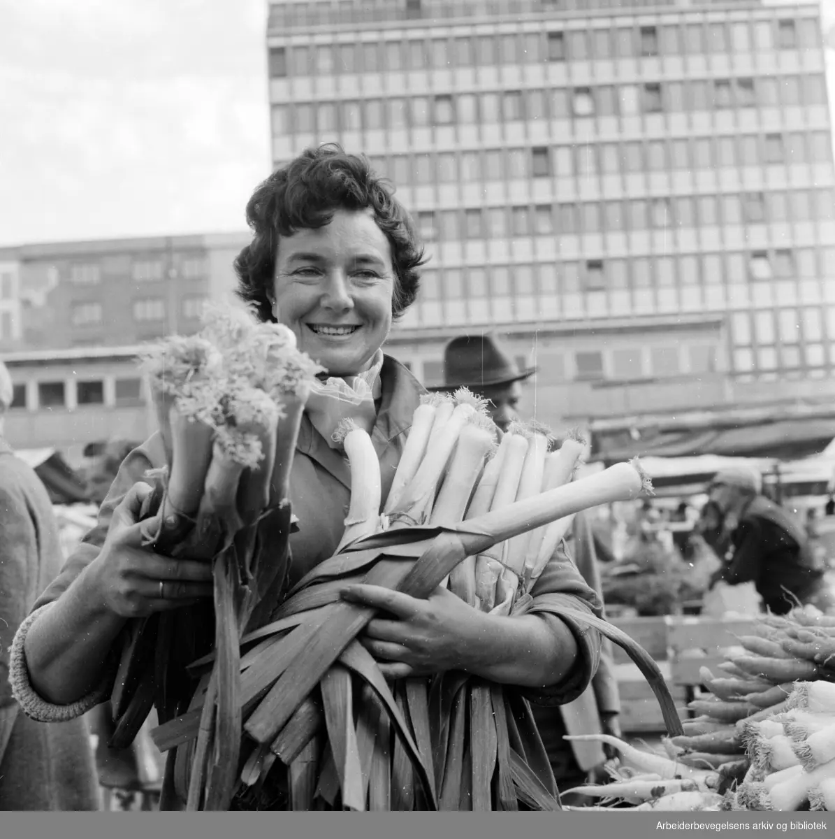 Youngstorget: Torgsalg. En dame viser fram purre fra torget. September 1959