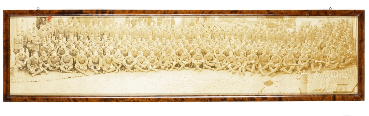 Fotografi med brun träram föreställande soldaterna i "28TH INFANTRY DIVISION A.E.F. (American Expeditionary Forces) 109TH INFANTRY REGIMENT, COMPANY K, BAGNEUX, FRANCE, MARCH 2ND, 1919". Fotografiet är även märkt med det fotograferande bolagets namn "Ewing Inc. No 1048 LITTLE ROCK, ARK." Fotografiet är taget när soldaterna är redo för hemfärd till USA från Bagneux, Frankrike.