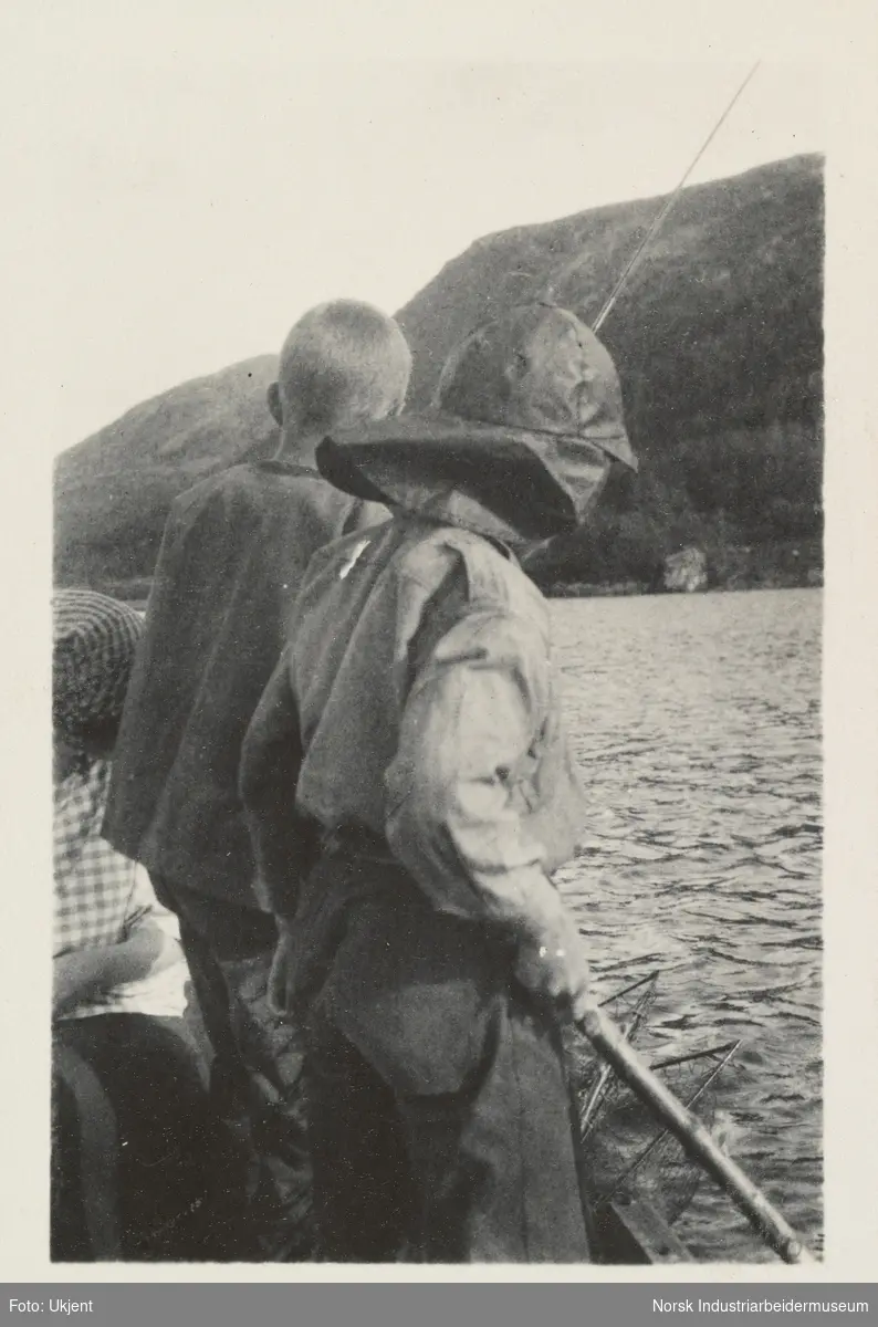 Briskeroe, Møsstrond. To gutter og en kvinne fisker i Møsvatn. Den ene gutten holder en fiskestang, mens den andre, iført en sydvest holder en pinne. I vannet sees en hov.