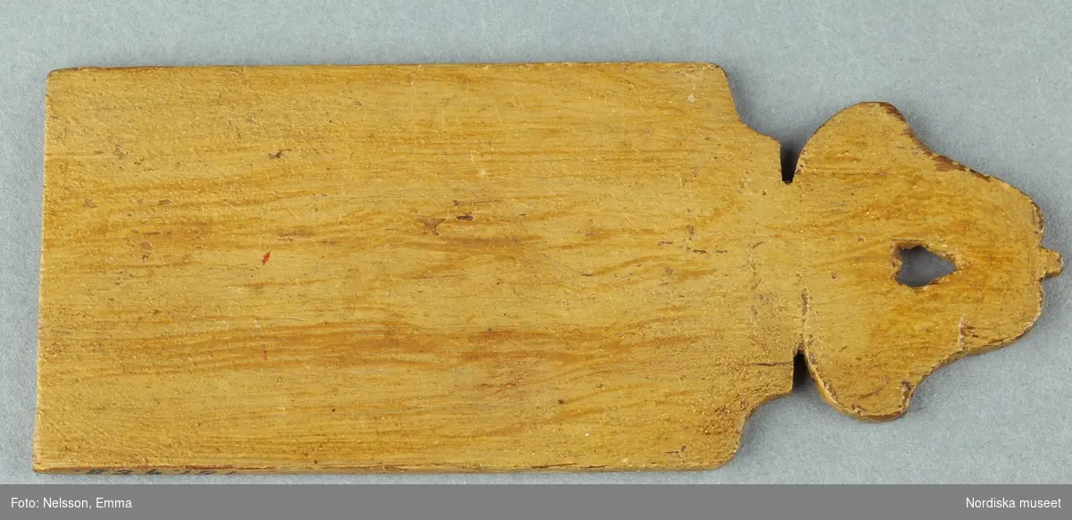 Inventering Sesam 1996-1999:
L 11 (cm)
Skärbräda, dockskåpsskärbräda, av trä, målad i gulaktig träådring, rektangulär, med profilerad ände.
Hör till dockskåp 151.825.
Bilaga
Anna Womack 1996