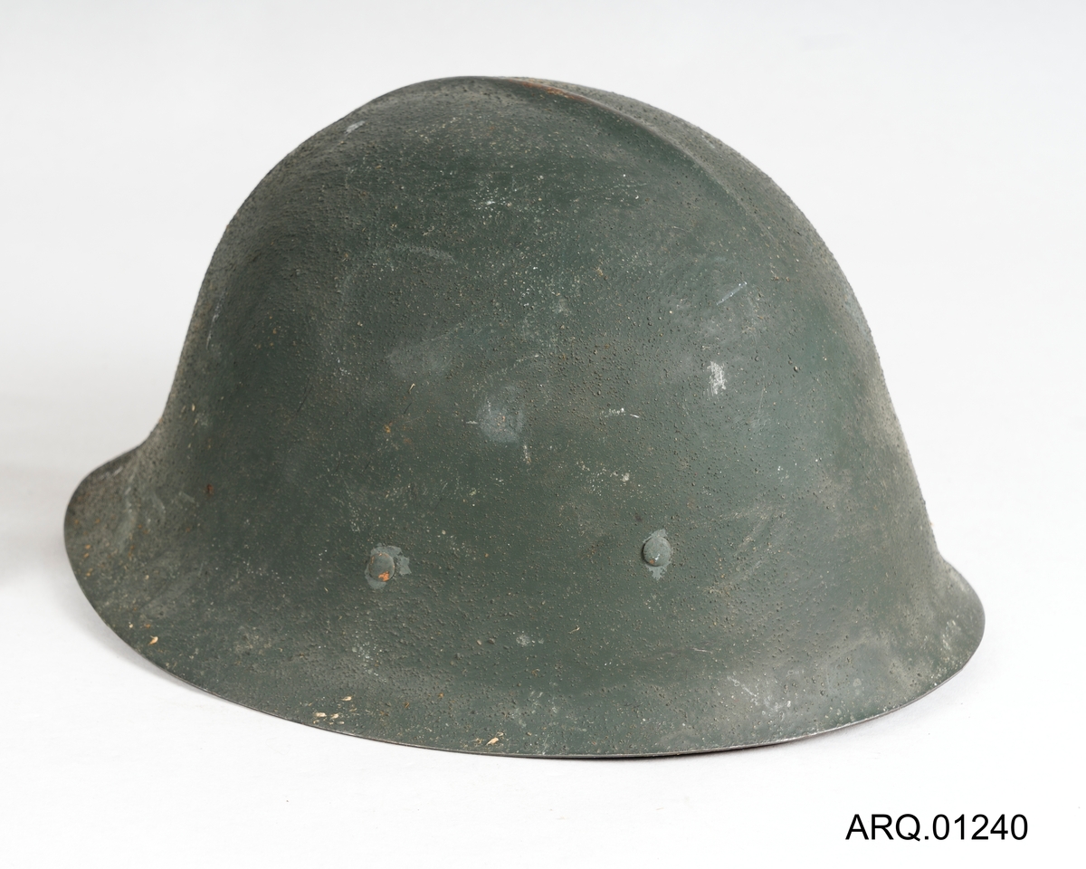 En Olivengrønn stålhjelm med skinninnlegg, festestropp i skinn med metallspenne og en stål-brem på innsiden av hjelmen.