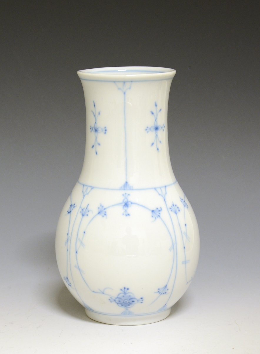 Vase i porselen, med nokså bred hals. Hvit glasur. 
Dekor: Stråmønster i blått, malt av Olav Steinsland.
Modell: Leif Helge Enger